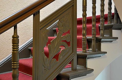 Herrschaftliches Treppenhaus mit hölzernem Geländer und rotem Teppich.